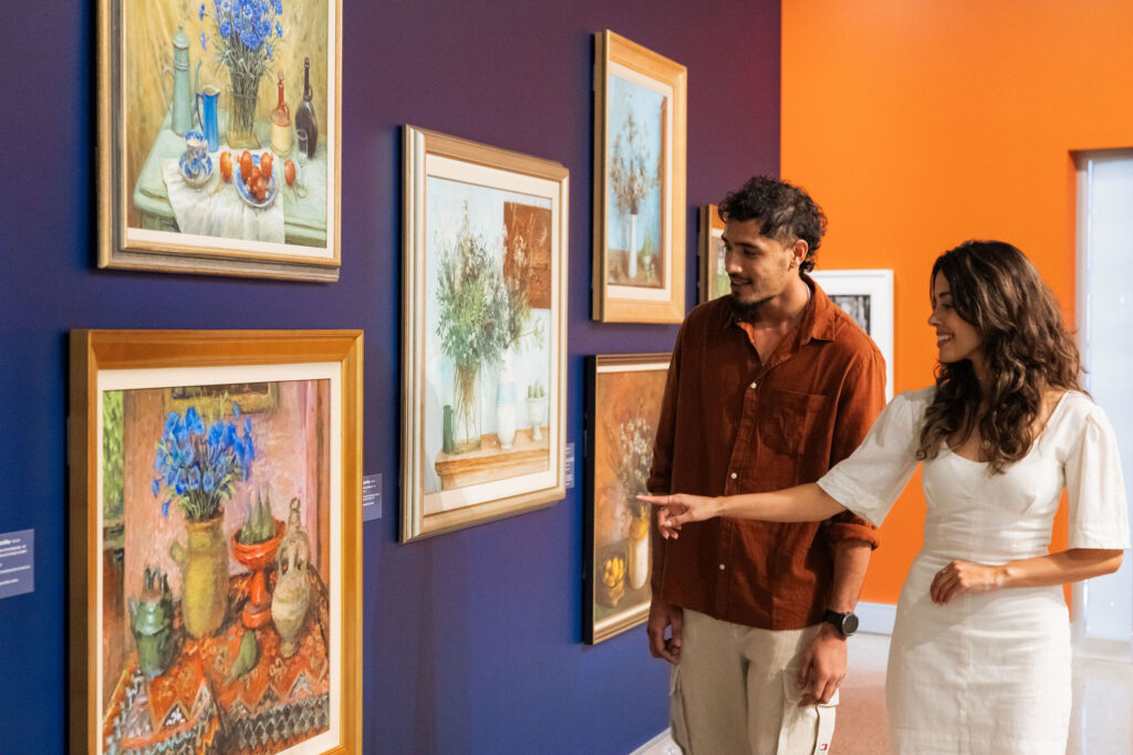 couple admire Margaret Olley artworks on dark blue wall