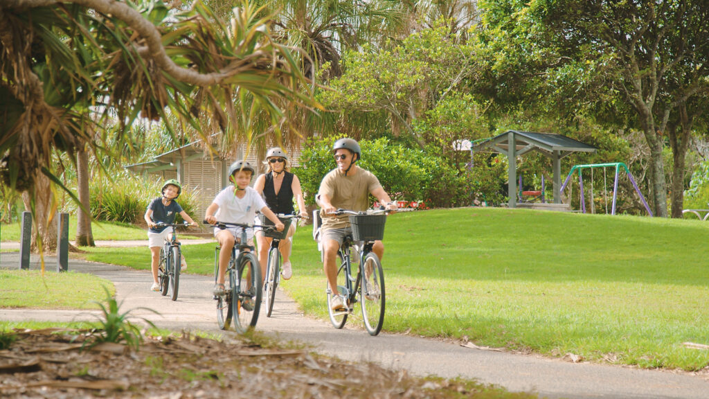 family ride bikes through park in kingscliff