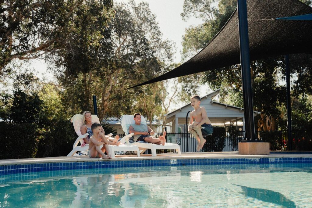 parents lay by pool on chairs while kids jump into the pool