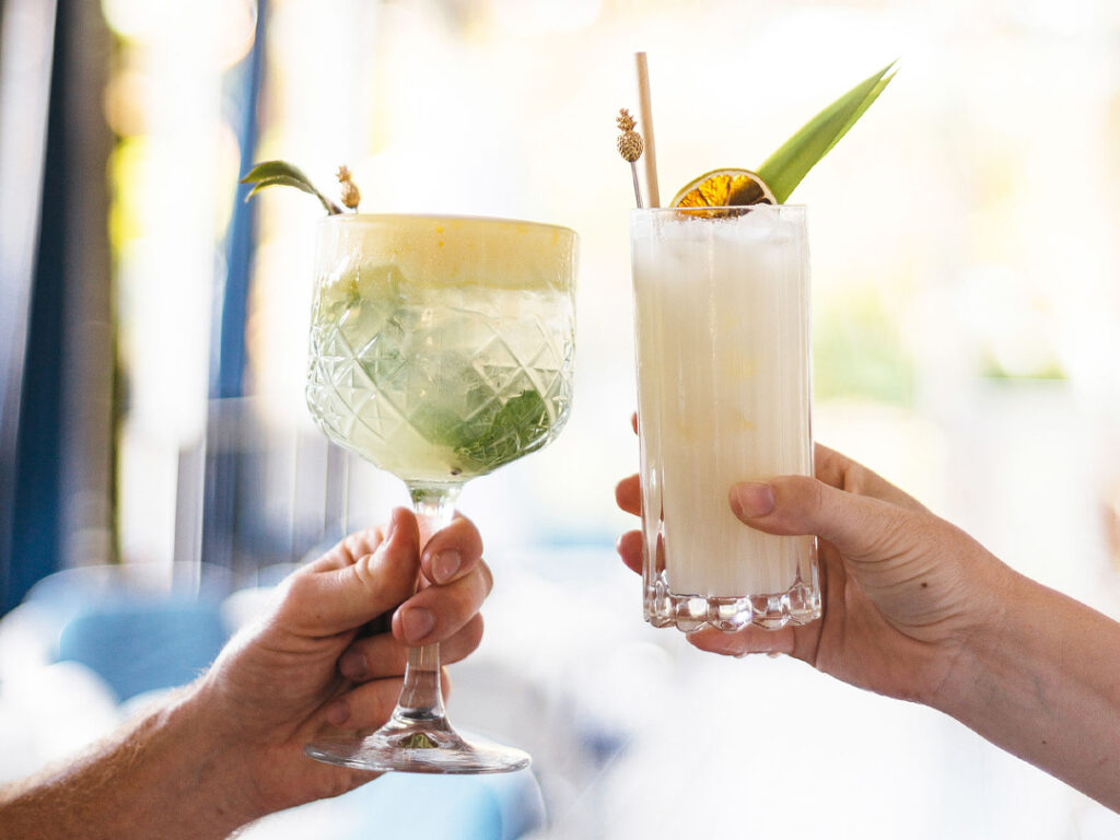 one cocktail with passionfruit foam and one pina colada cocktail in tall glass