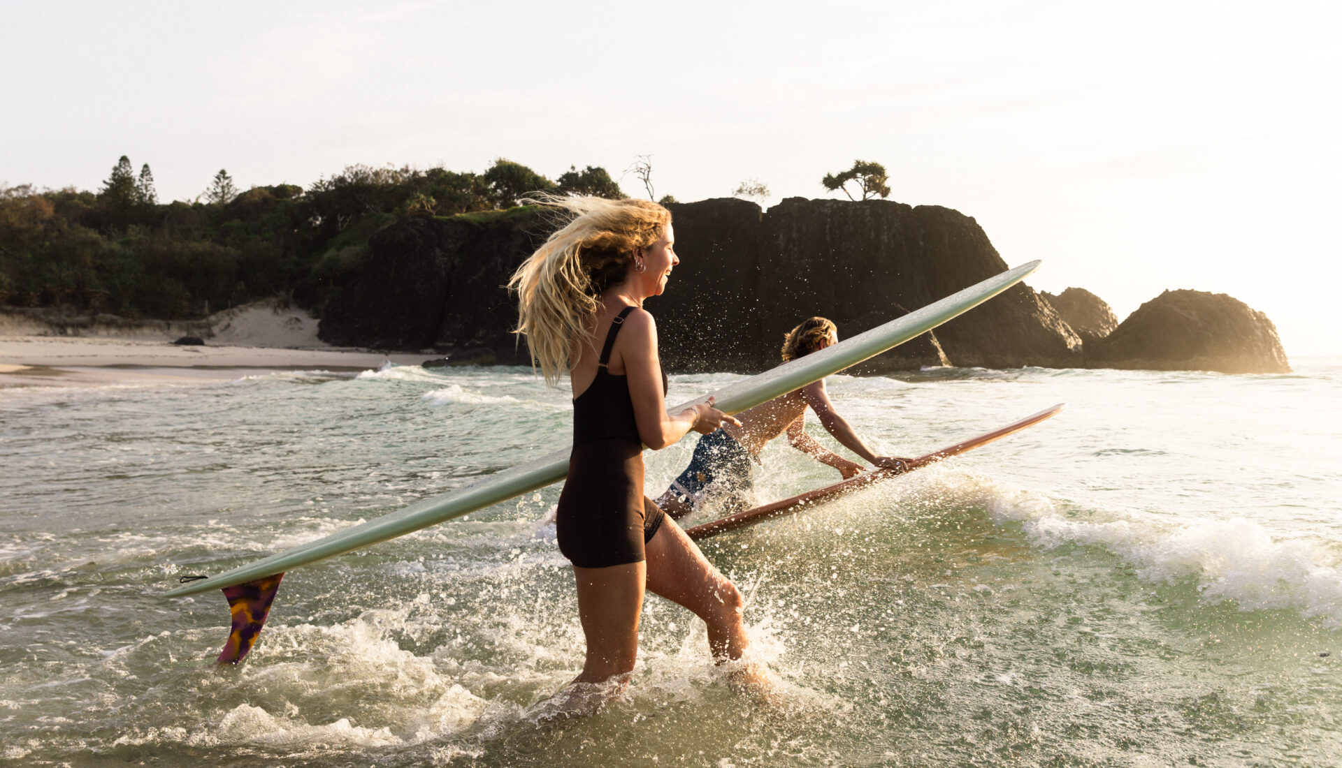 couple running into surf with surfboards