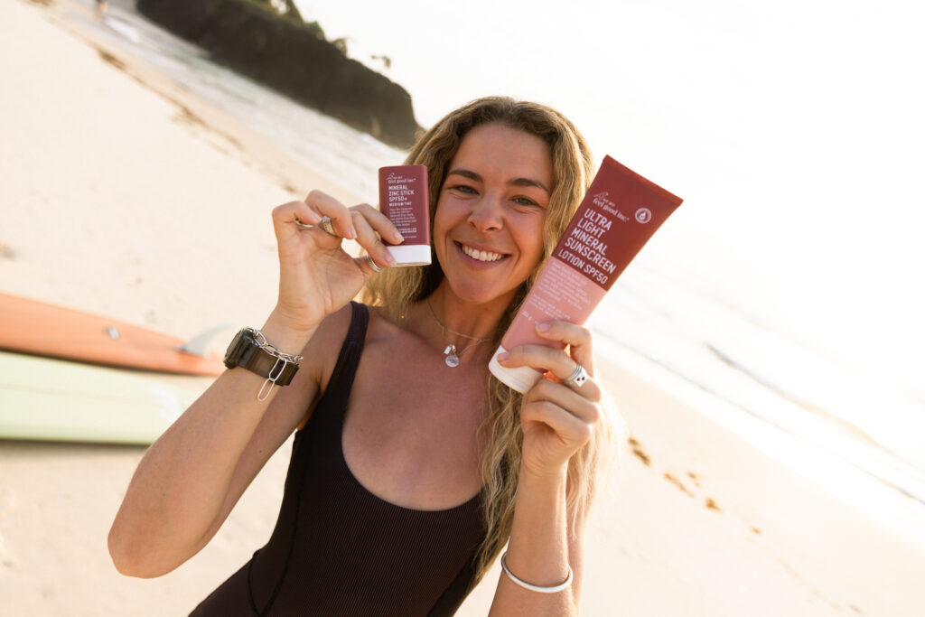 girl smiles holding two we are feel good inc sunscreens on beach